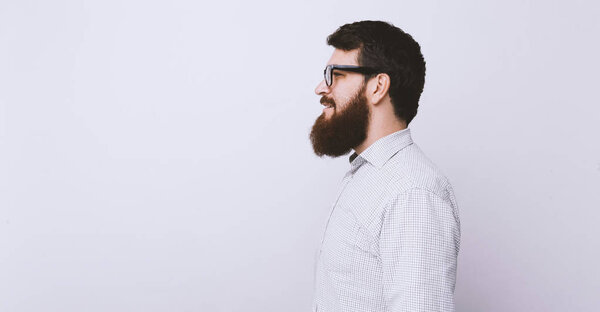 Half face view of young bearded hipster in shirt isolated on light gray background