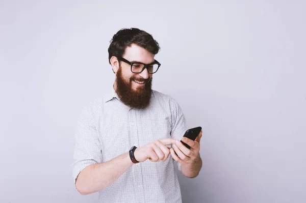 Cheerful Bearded Young Man Typing His Mobile Light Gray Background — Stock Photo, Image