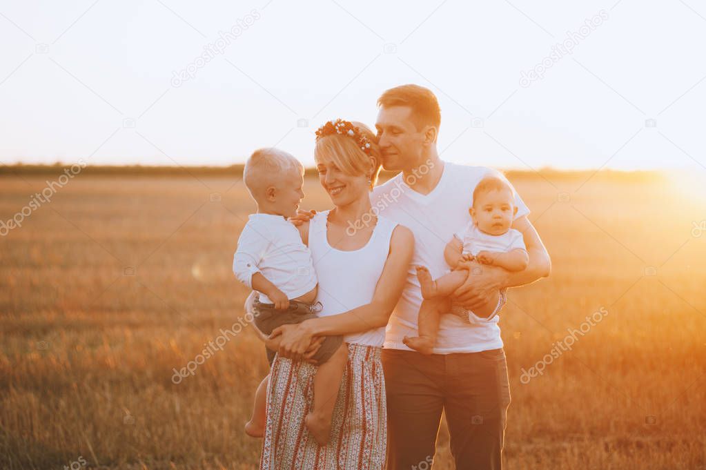 Happy young family holding their children on hands on nature in field on sunset