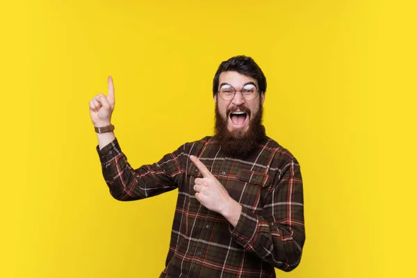 Handsome excited bearded man pointing away at copy space and looking at the camera