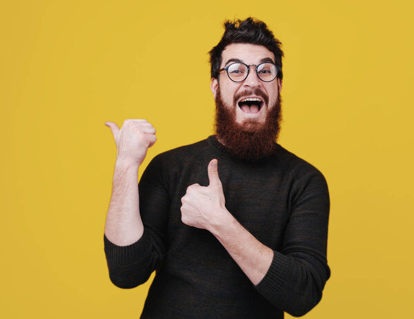 Portrait of excited bearded man gesturing thumbs up  and showing at copy space