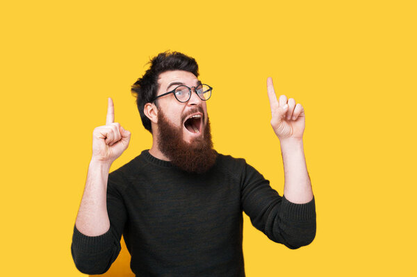 Handsome excited hipster guy in glasses showing up with fingers and looking away