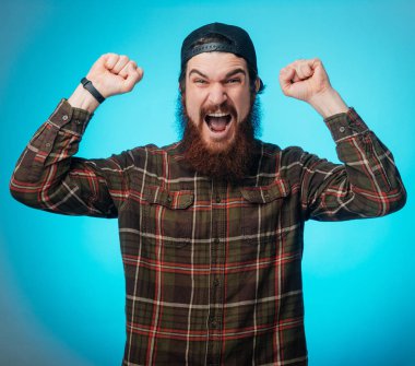 Kırmızı kareli gömlek giyen sakallı mutlu hipster adam fotoğrafı üzerinde izole mavi arka plan exults