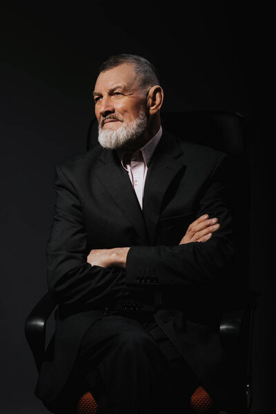 Portrait of a stylish handsome mature bearded man on a armchair with crossed hands. Fashion shot. Men's clothing 