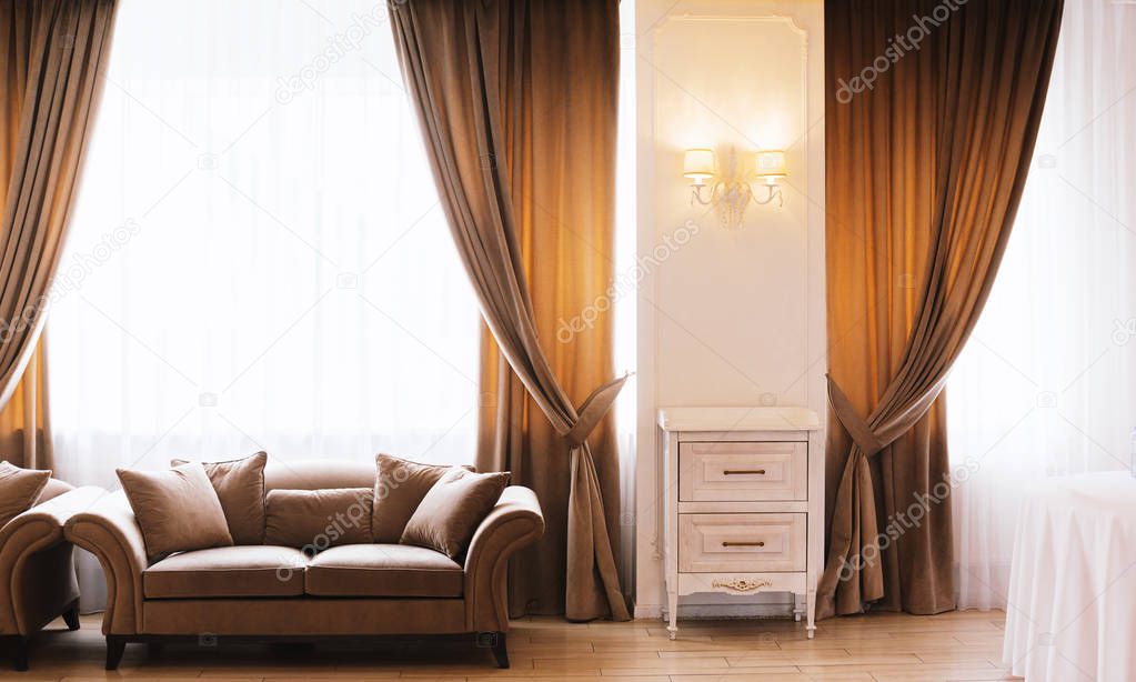 Photo of hotel room or restaurant with elegant curtains, and sofas, big windows, with vintage lamp on wall 