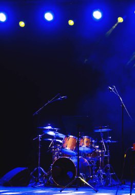 Empty illuminated stage with drumkit, guitar and microphones clipart