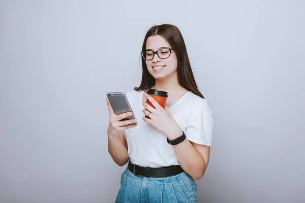 Sorrindo menina usando óculos está usando telefone e segurando um ta vermelho — Fotografia de Stock