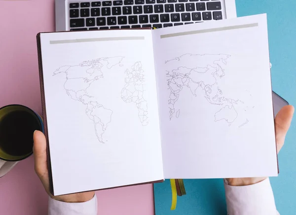 Flat lay concept. Opened notebook with world map, handsomea woman hollding his notebook on work desk background