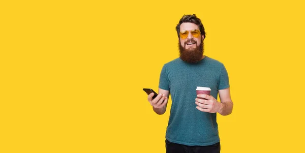 英俊的胡须男子手里拿着咖啡和电话 Hipster 在时尚的黄色眼镜在被隔绝的背景 — 图库照片