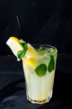 Koyu arka planda limon dilimi ve nane yaprakları ile klasik buzlu limonataya sahip bir cam
