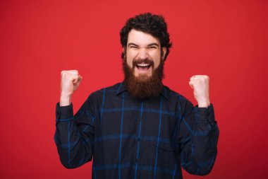 Yumrukları ile neşeli sakallı adam, kırmızı duvar arka planda kazanan 