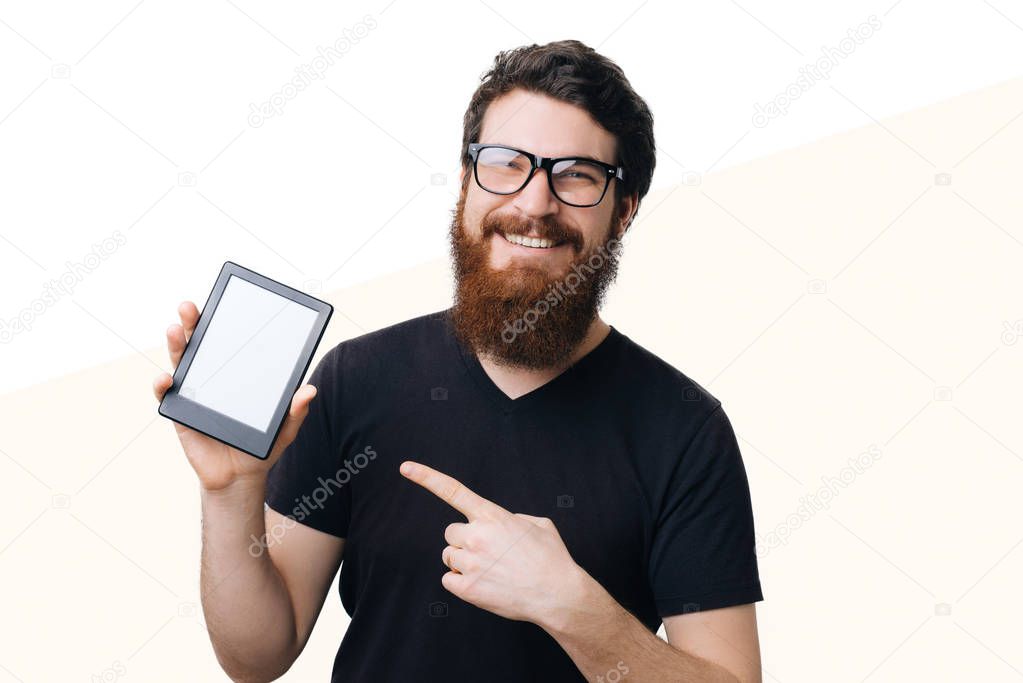 Photo of handsome bearded nerd pointing at his new little tablet over isolated background 