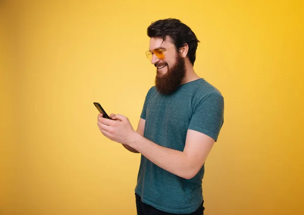 Photo Bearded Man Stylish Glasses Using Smartphone Yellow Background — Stock Photo, Image