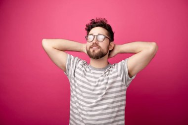 Gözlük takan, el ele tutuşan ve pembe arka plana bakan mutlu genç adam. 