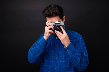 Mavi shrt yakışıklı genç adam, üzerinde vintage kamera ile bir fotoğraf çekmek, karanlık arka plan 