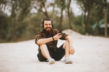 Mutlu sakallı sakallı adam, plaj kum otururken kulaklık ile müzik dinliyor