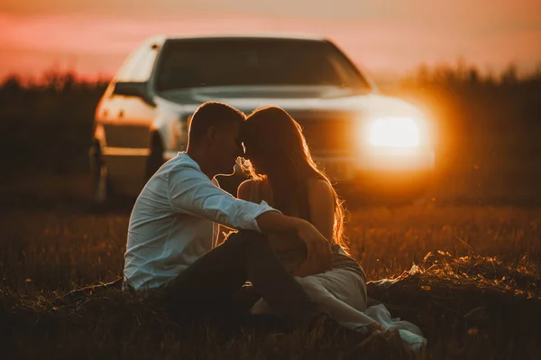 A beautiful photo of a couple siiting in field on sunset, on car light background