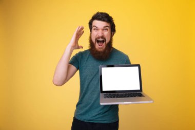 Sakallı heyecanlı adam bir dizüstü bilgisayar, sarı arka plan üzerinde kamera hayran bir seyir olding olduğunu 