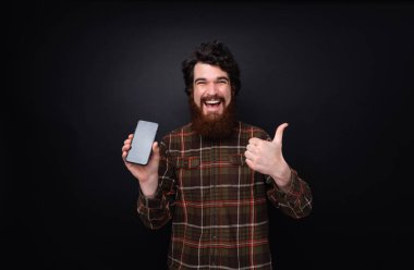 Başparmak uo ve yeni cep gösteren neşeli adam fotoğrafı, karanlık duvar üzerinde ayakta