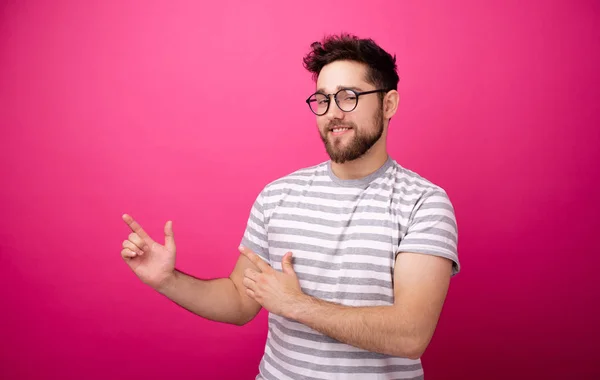 Photo of handsome bearded young man  pointing away over pink isolated background