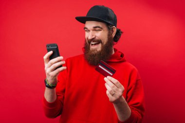 İzole arka plan üzerinde, bir akıllı telefon ve kredi kartı kullanarak Mutlu sakallı adam  