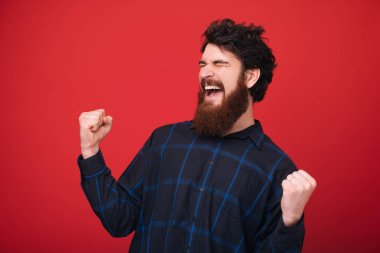 Sakallı adam gözlerini kapatıyor ve kırmızı arka plan üzerinde yükselmiş elleriyle kutluyor 