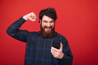 Kazanan bir jest gibi, akıllı telefon ve yükselen el kullanarak kırmızı arka plan üzerinde sakallı bir adam