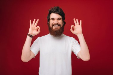 Ok işareti gösteren kırmızı arka plan üzerinde beyaz tshirt yakışıklı sakallı adam 
