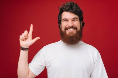 Beyaz tshirt yakışıklı bir sakallı adam fotoğrafı, gülümseyen ve yukarı işaret, kırmızı arka plan üzerinde 