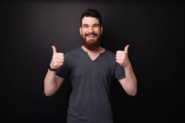 Koyu arka plan üzerinde başparmak gösteren dişli gülümseyen sakallı bir adamın fotoğrafı 