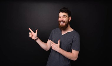 Gri tshirt neşeli sakallı adam kamera loking sırasında uzağa işaret 
