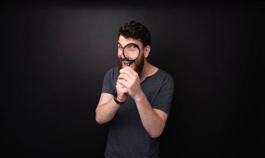 Karanlık arka plan üzerinde büyüteç ile eğlenen sakallı bir adamın fotoğrafı  