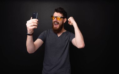 Heyecanlı sakallı adam mobil tutan fotoğraf, scraming ve yükselen elleri ile celebraing