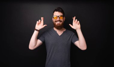 Sakallı genç adamın karanlık arka plan üzerinde duran daha fazla şans için parmakgeçiş fotoğrafı 