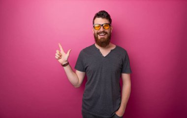 Neşeli sakallı adam parmakla işaret, pembe arka plan üzerinde 
