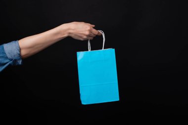 Siyah arka planda mavi alışveriş çantası tutan bir kadın.