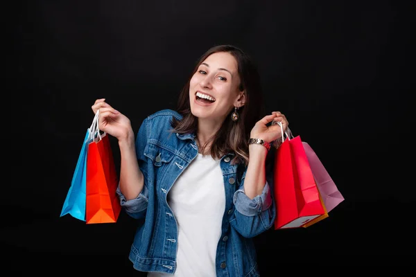 Glad ung kvinna leende och hålla shoppingväskor över svart bakgrund — Stockfoto