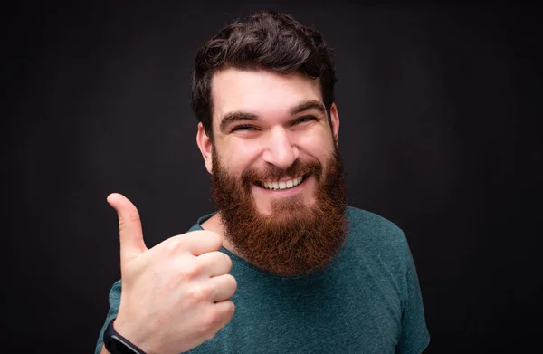 Portrait en gros plan d'un hipster barbu souriant montrant les pouces debout sur fond noir — Photo