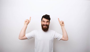 Beyaz tişört içinde sakal ile heyecanlı gülümseyen adam fotoğraf boşaltmak yukarı işaret