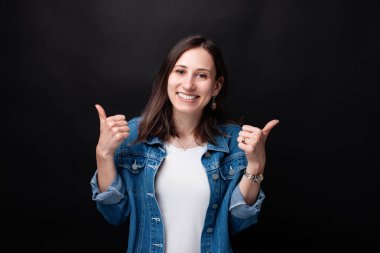 Karanlık arka planda başparmak yukarı gösteren neşeli genç kadının portre yakın