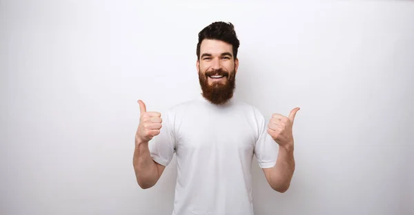 Портрет красивого и взволнованного бородатого мужчины с большими пальцами над белой стеной — стоковое фото
