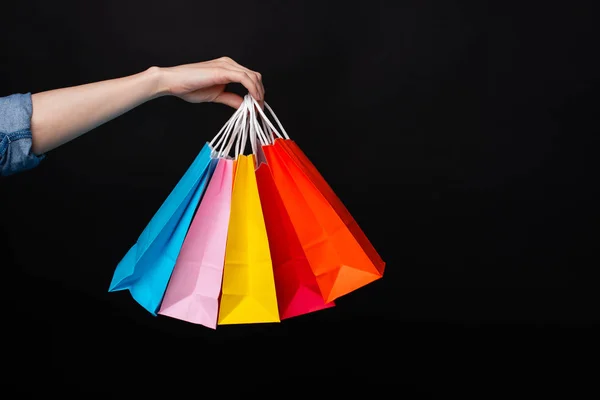 Mujer mano sosteniendo coloridas bolsas de compras sobre fondo oscuro —  Fotos de Stock