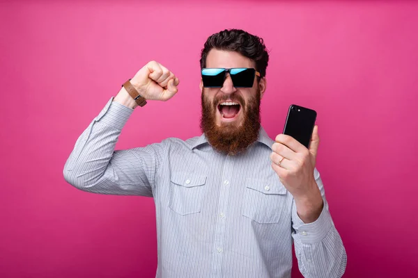 Foto de un hombre barbudo sorprendido en un smartphone casual y celebrando la victoria — Foto de Stock