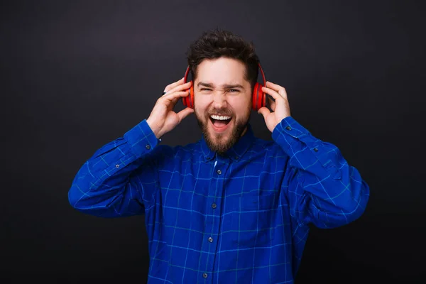 Beau jeune homme barbu écoutant la musique sur écouteurs et chantant sur fond noir . — Photo