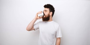 Genç sakallı adam beyaz arka plandaki kağıt bardaktan kahve ya da çay içiyor. Kahveyi götür.. 