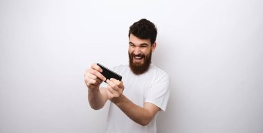 Genç sakallı adam beyaz arka planda telefonunu çalıyor..