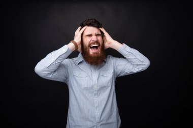 Yakışıklı sinirli sakallı adam elleri başında ve karanlık izole arka plan üzerinde çığlık