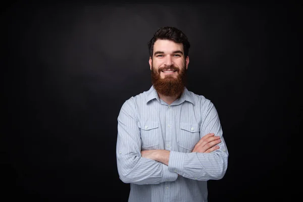 Porträt eines fröhlichen bärtigen Mannes, der mit verschränkten Armen vor dunkelgrauem Hintergrund lächelt — Stockfoto