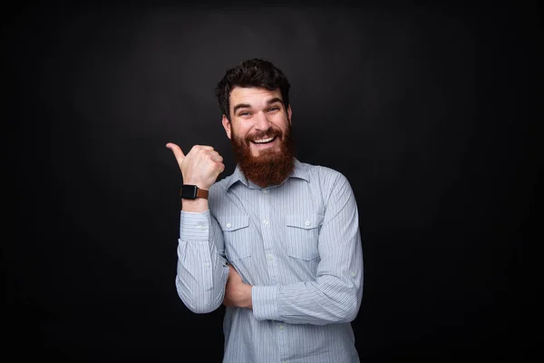 Foto del hombre barbudo mostrando el pulgar hacia arriba y sonriendo a la cámara sobre el oscuro terreno de bcakground aislado —  Fotos de Stock