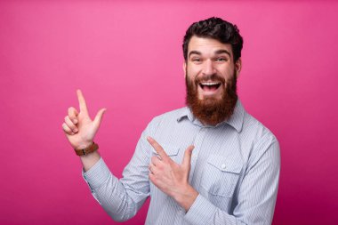 Genç sakallı hippi puanları, iki eli havada ve pembe arka planda..